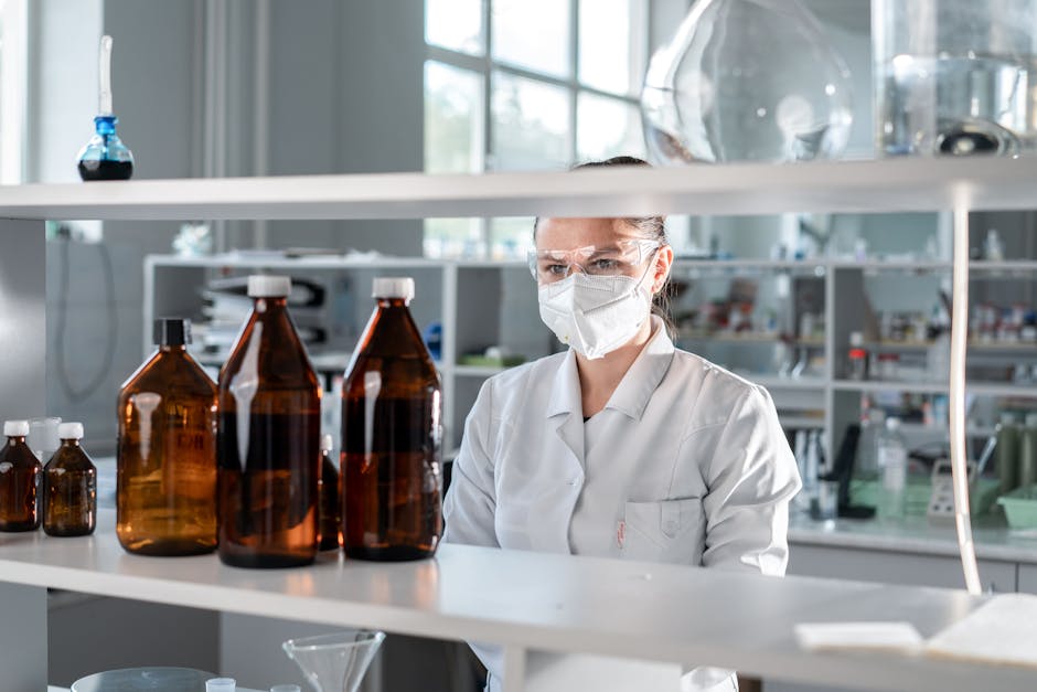 A female scientist wearing protective gear and examining chemical bottles in a laboratory setting.