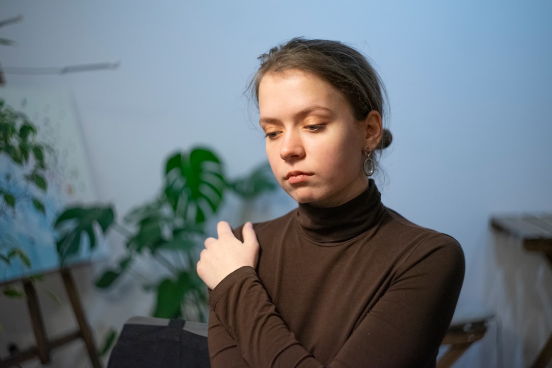 Young woman in brown turtleneck looking down thoughtfully.