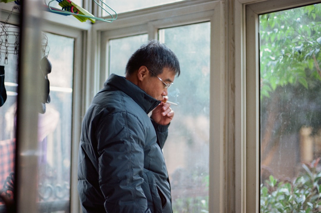 A man standing in front of a window smoking a cigarette