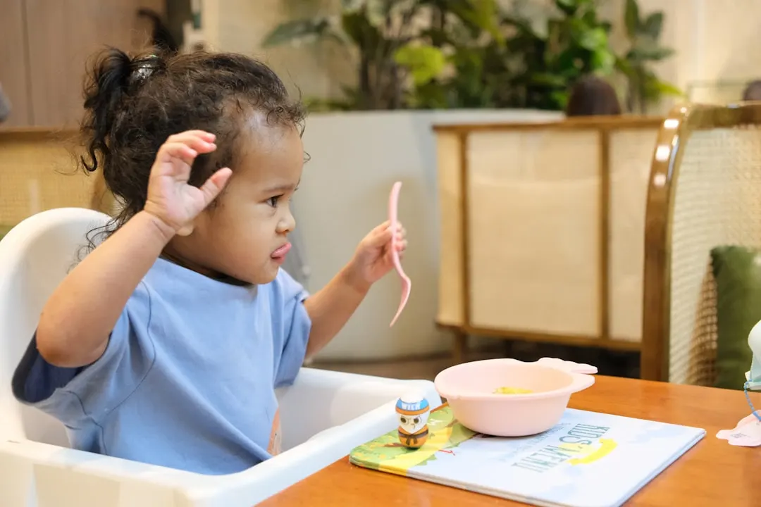 Young child in high chair with spoon and bowl.