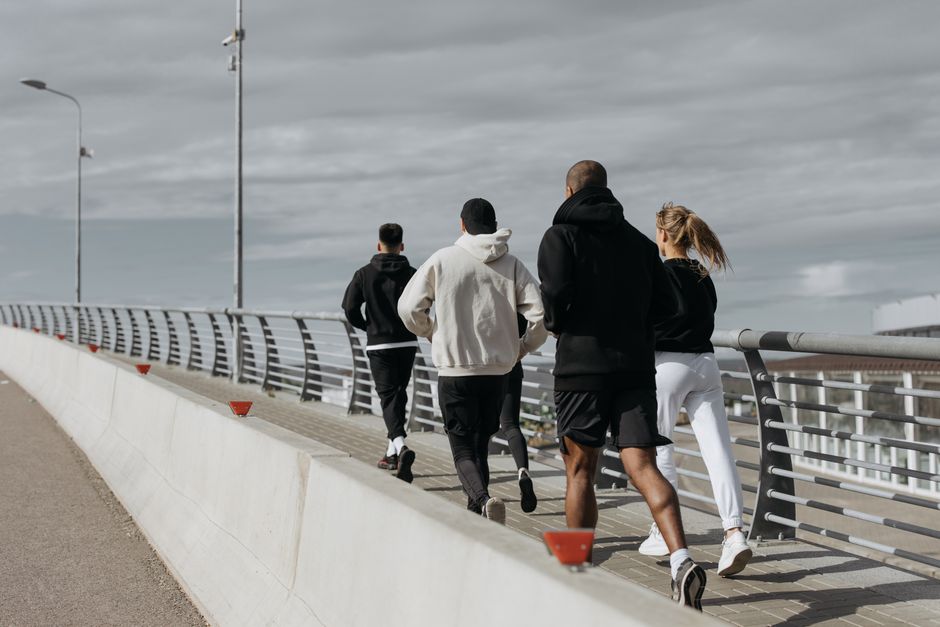 A diverse group of adults jogging together on a city bridge during the day.
