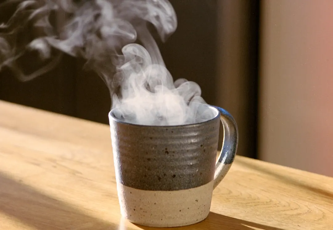 A steaming mug of hot beverage on a wooden table.